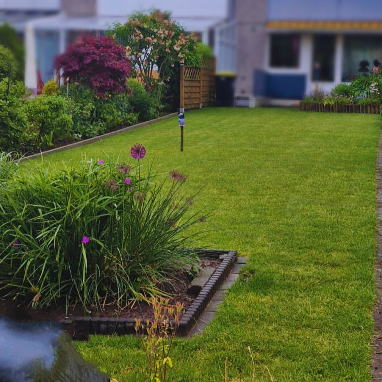 Grüner Garten mit Blumenbeeten und gepflegtem Rasen hinter einem Wohngebäude.